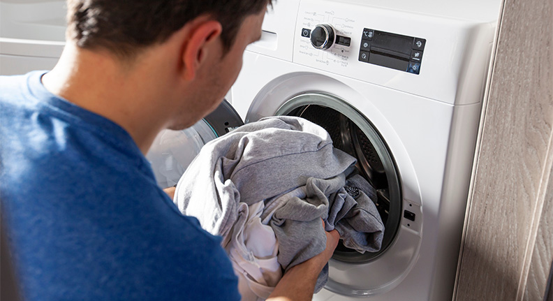 homem colocando as roupas na máquina de lavar roupa