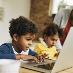 crianças na cozinha com a mãe usando dispositivos eletrônicos que fazem parte de suas rotinas