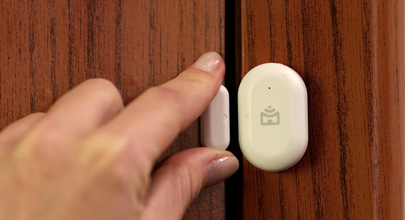 mulher instalando um sensor de abertura smart da Positivo Casa Inteligente na porta de sua casa