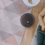 homem deitado no sofá enquanto o Smart Robô Aspirador Wi-fi Laser da Positivo Casa Inteligente aspira o chão da sala